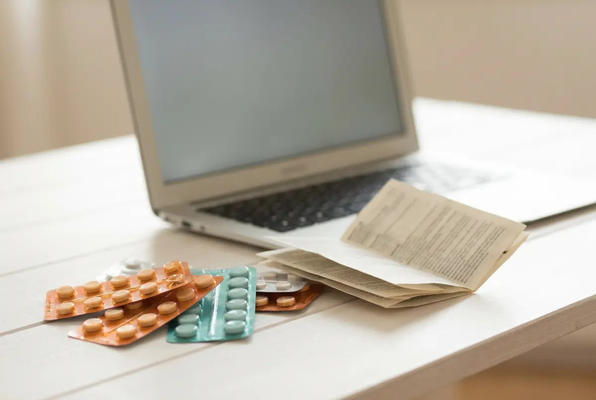 Plaquettes de médicaments et une notice à côté d'un ordinateur portable